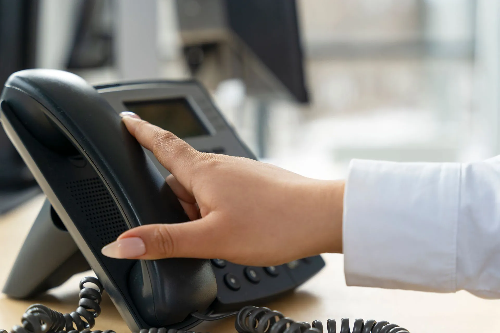 Hand reaching for a black office phone receiver on a desk. telecommunication equipment in Halfmoon NY